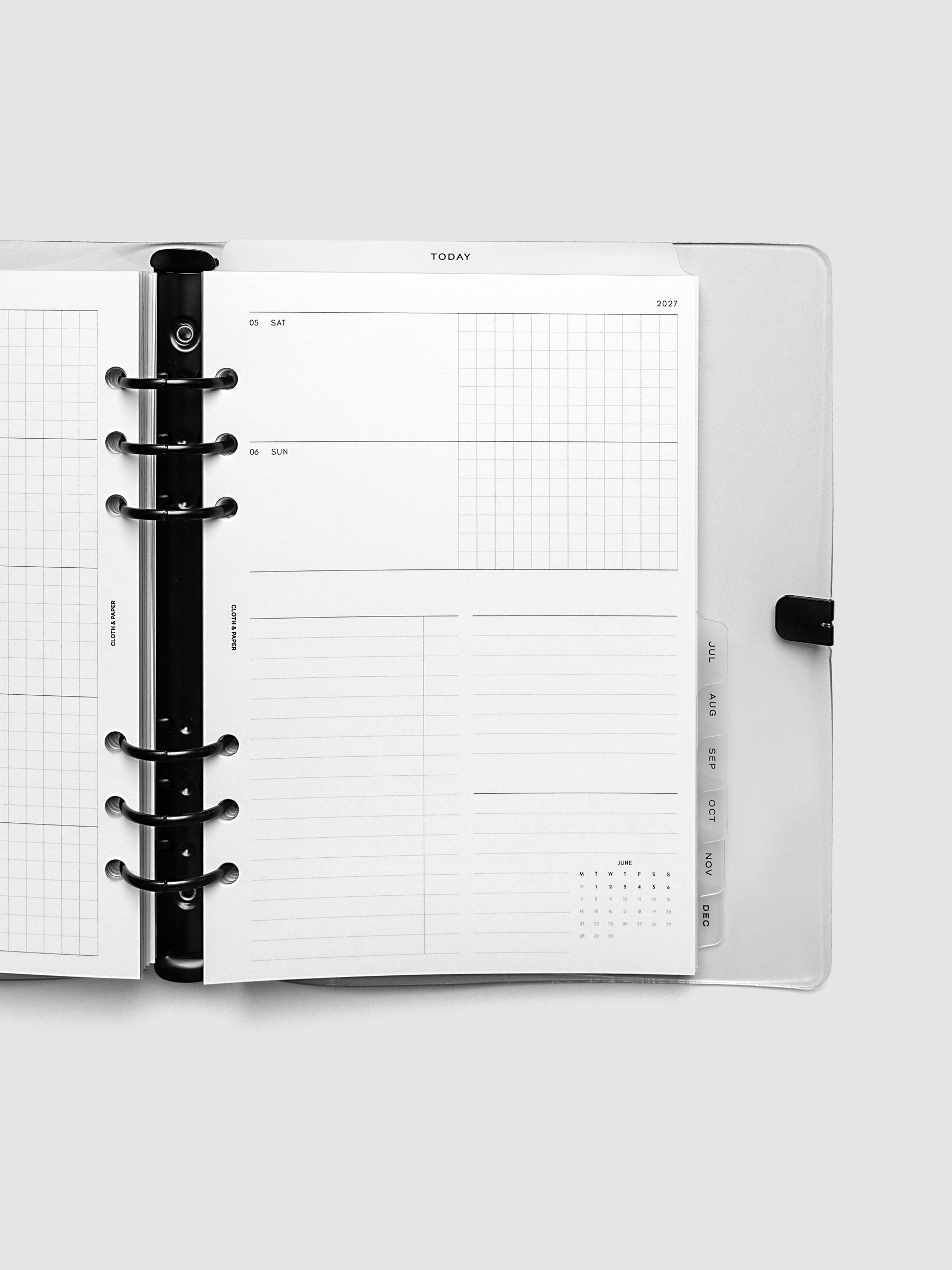 Close-up of an open planner with black 6-ring binding, weekly horizontal spread showing Saturday and Sunday in a shared row split into lined and graph columns, tabbed monthly dividers visible at the edge, A5 6-Ring Punch size
