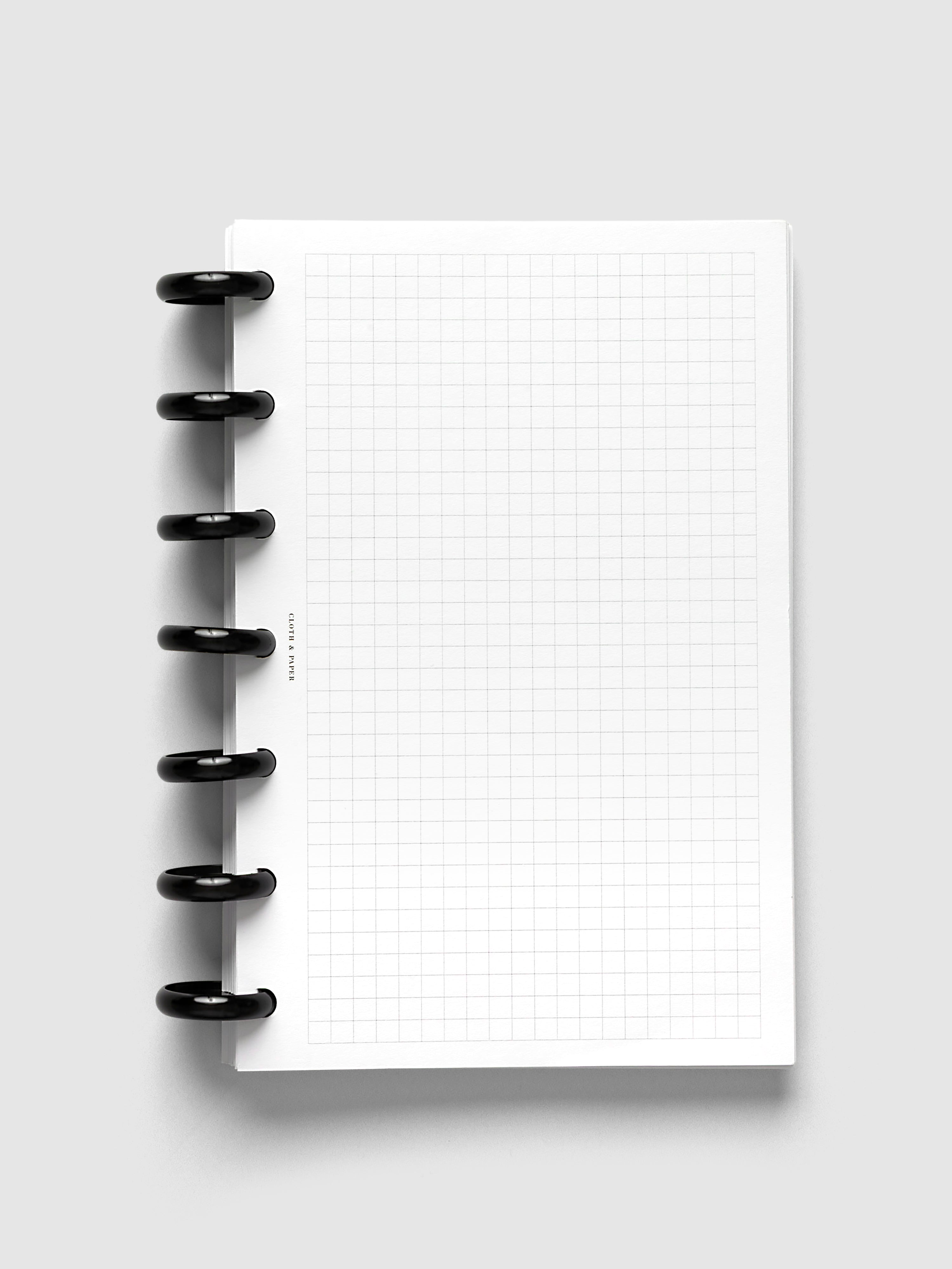 Aluminum Planner Discs | Black, 1 Inch, installed on a discbound planner with lined paper pages, close-up of six discs from the side