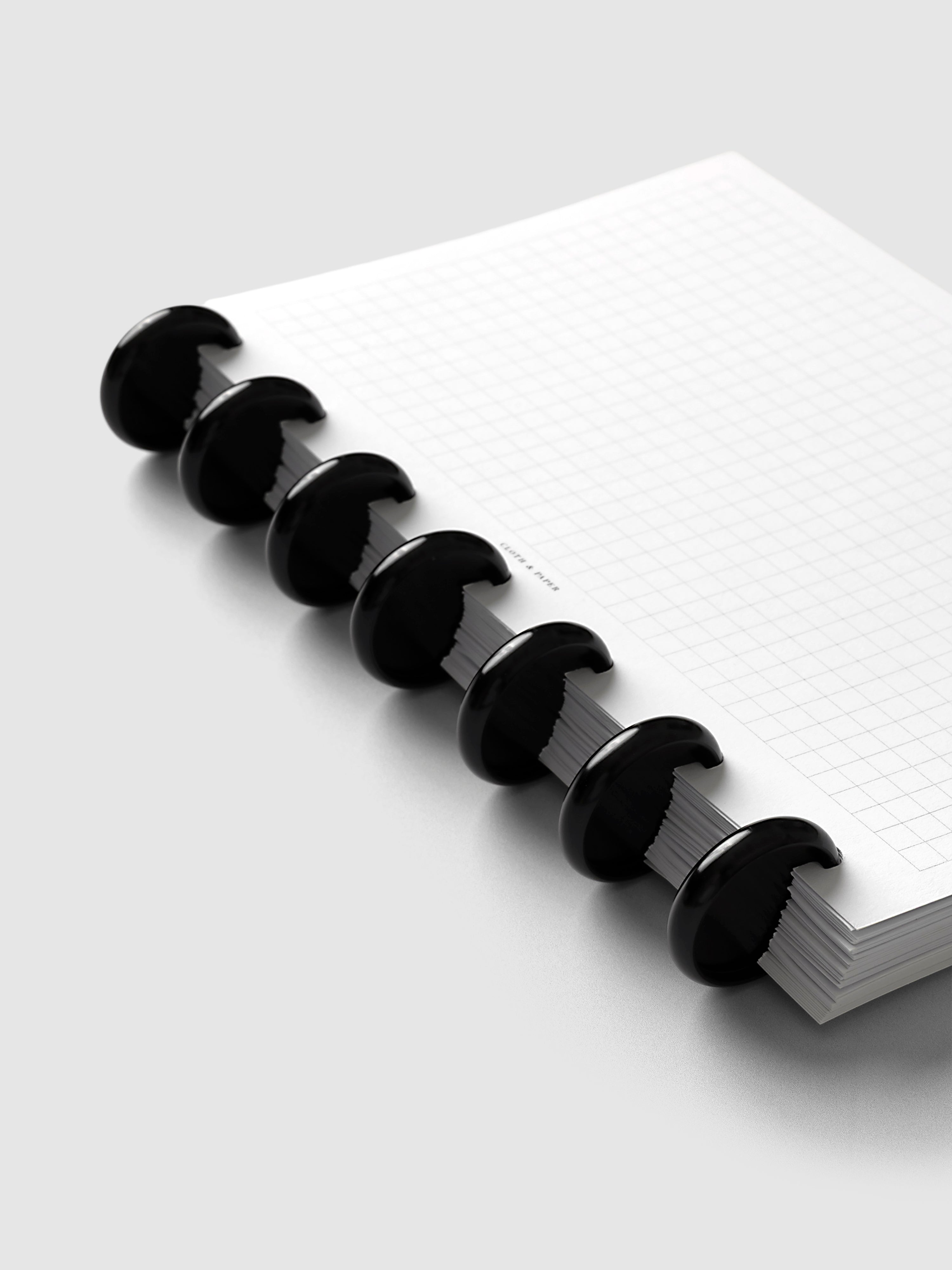 Aluminum Planner Discs | Black, 1 Inch, installed on a discbound planner showing eight discs holding graph paper pages, angled view