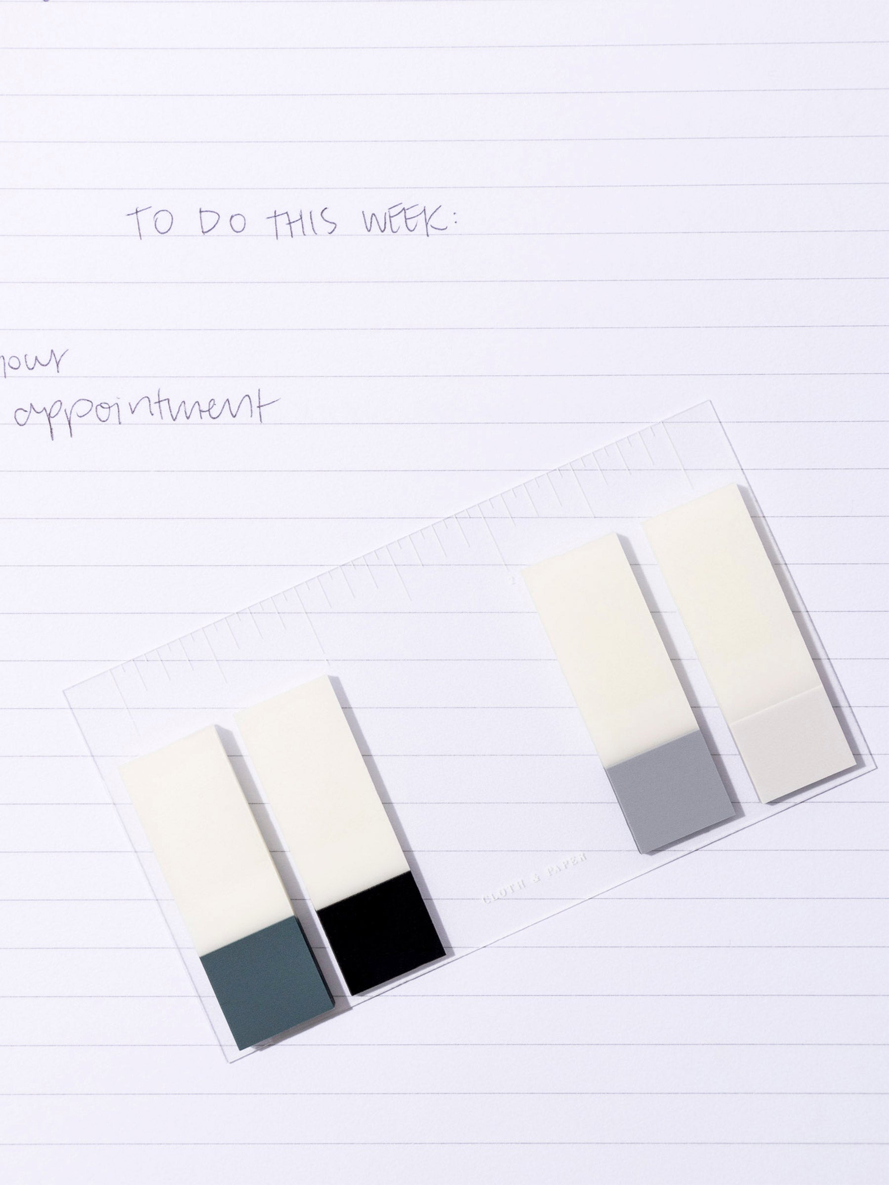 Clear journaling card shown with Matchstick Page Flags attached to it. The card rests on a notebook with a to-do checklist written inside of it.
