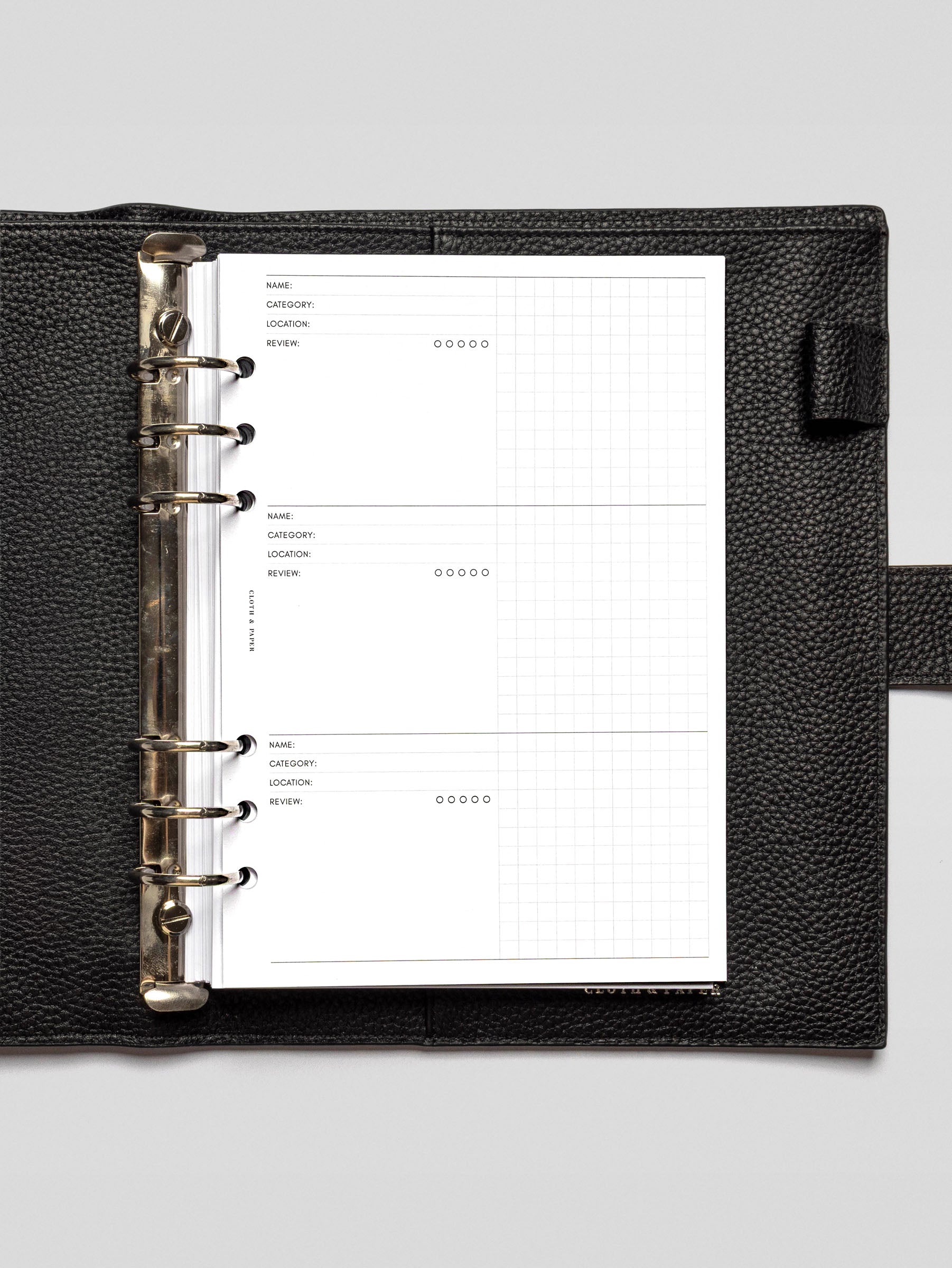 A close-up of the Experience Tracker Inserts in an open black leather planner binder, showing structured fields for Name, Category, Location, Review, and a 5-dot rating system, along with a right-hand grid section for notes.