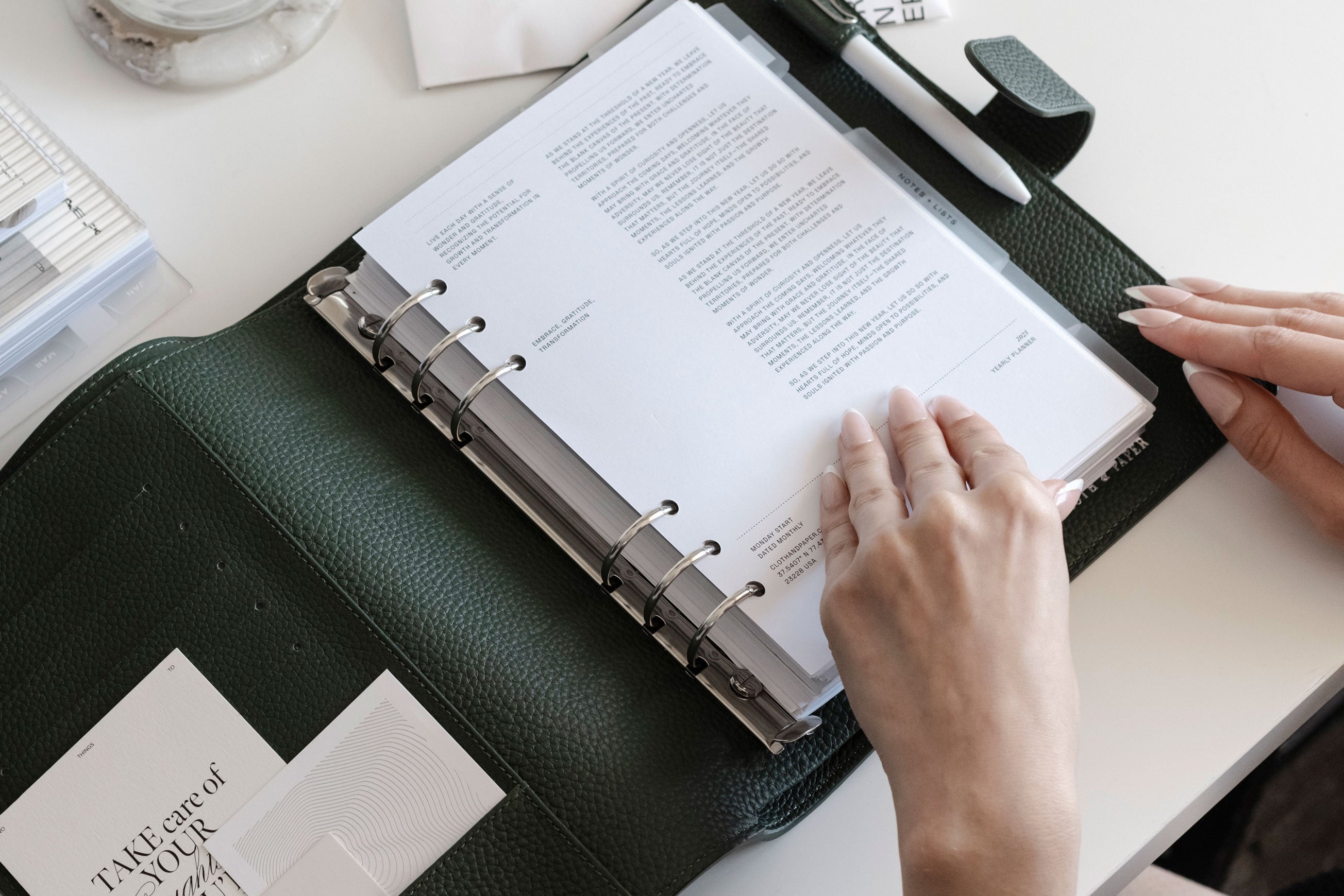 A Foundations Leather 6-Ring Agenda in A5 is opened on a white desk.  Two hands are beginning to flip through the pages inside.