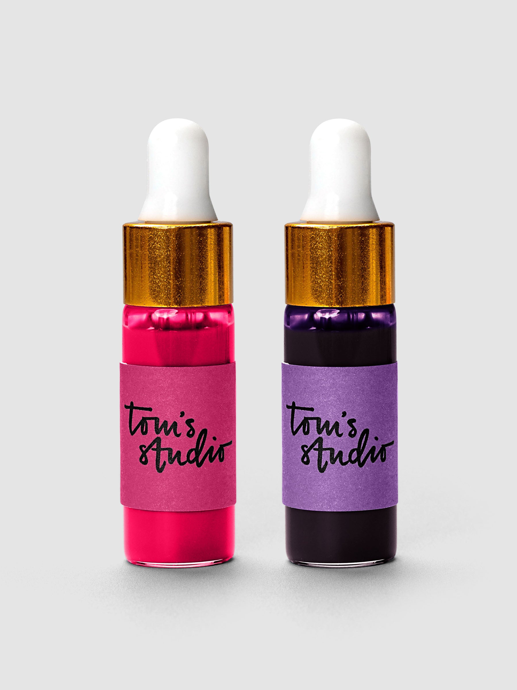 Two Tom's Studio ink bottles with gold caps and white droppers in pink and purple