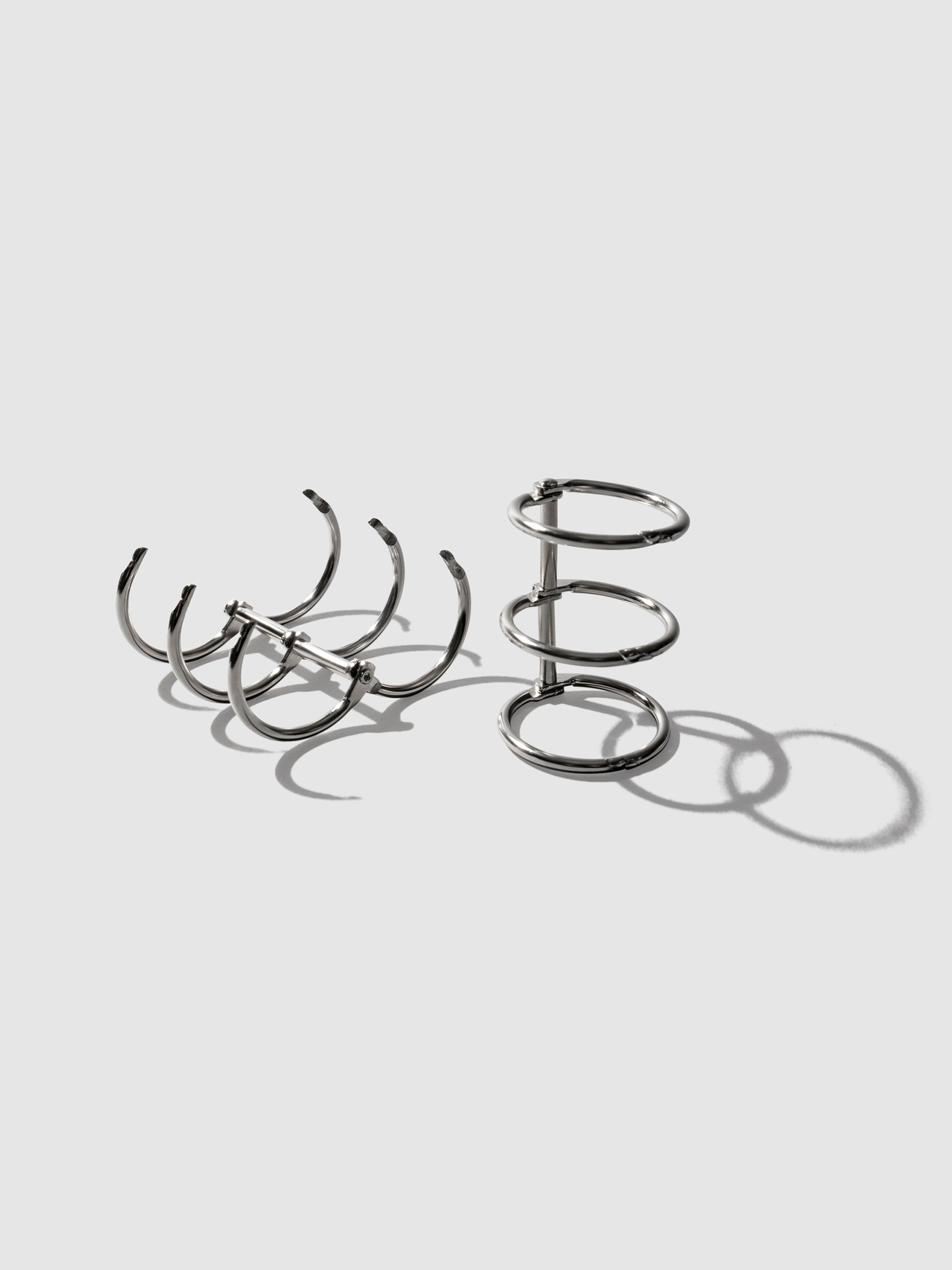 Silver rings displayed on a neutral background. One set is laid on its back and opened, the other is sat upright with rings closed.