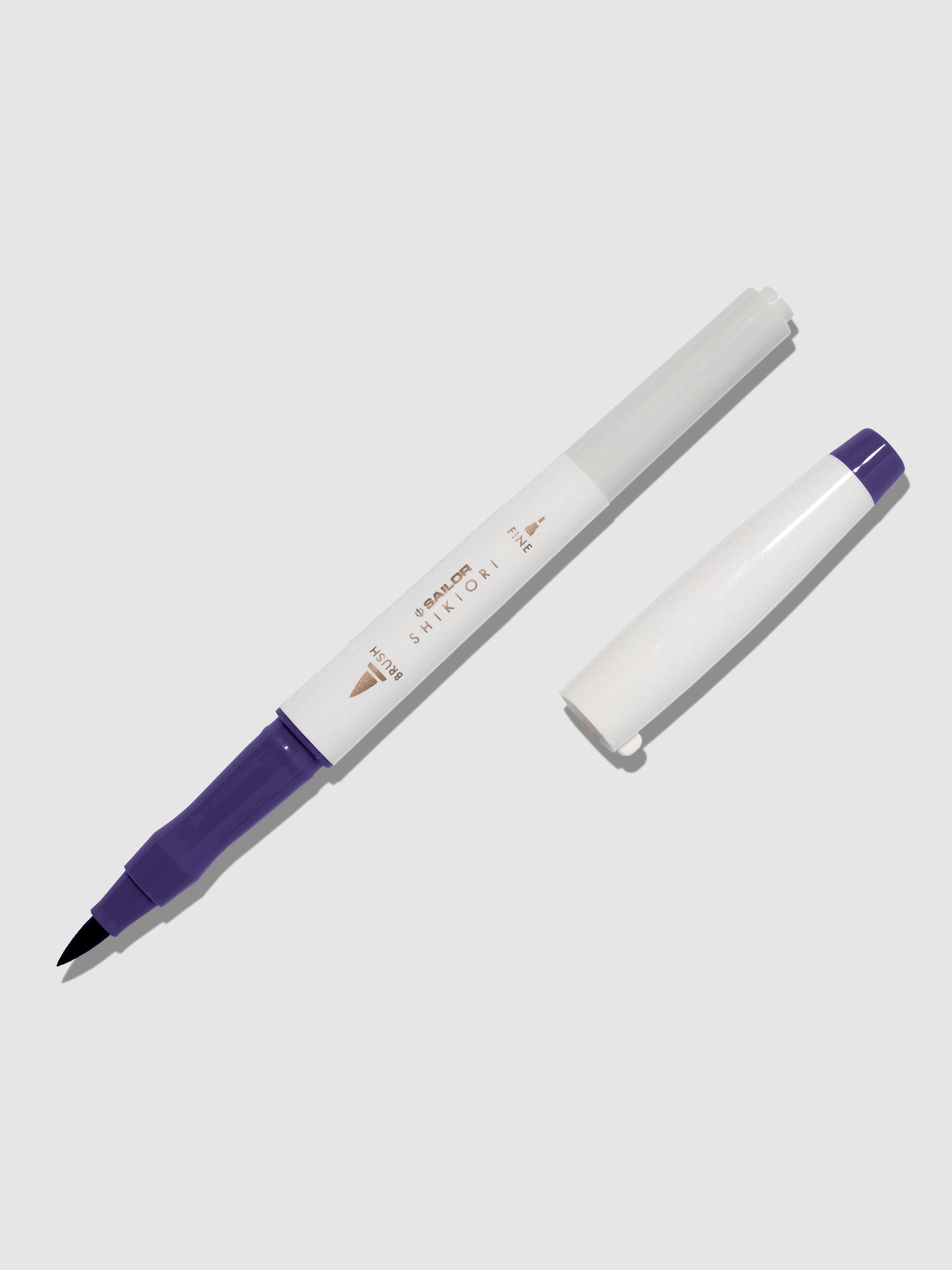 Brush pen displayed on a neutral background. It is uncapped with its brush nib exposed, and the cap lying parallel to the marker. Color pictured is Shigure. 