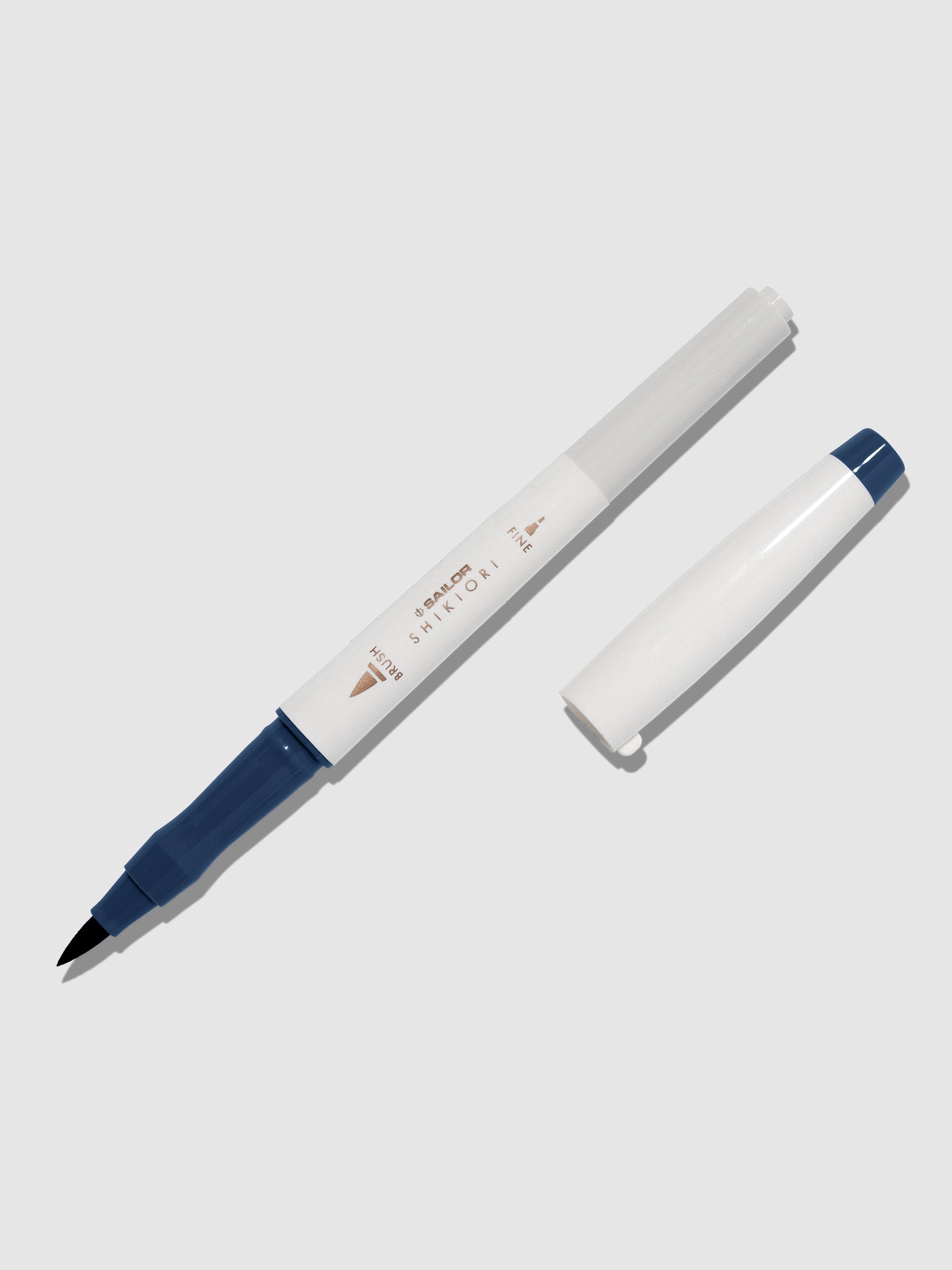 Brush pen displayed on a neutral background. It is uncapped with its brush nib exposed, and the cap lying parallel to the marker. Color pictured is Yonaga. 