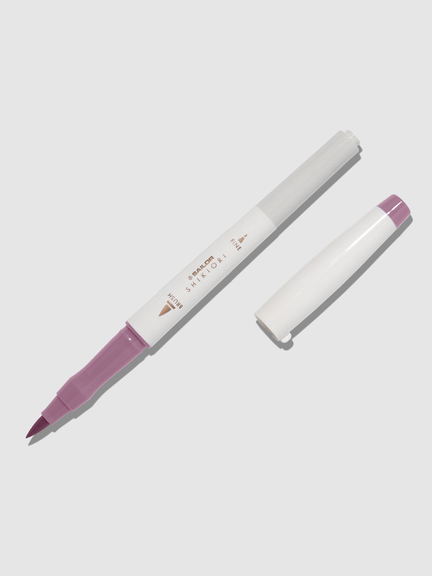 Brush pen displayed on a neutral background. It is uncapped with its brush nib exposed, and the cap lying parallel to the marker. Color pictured is Yozakura. 