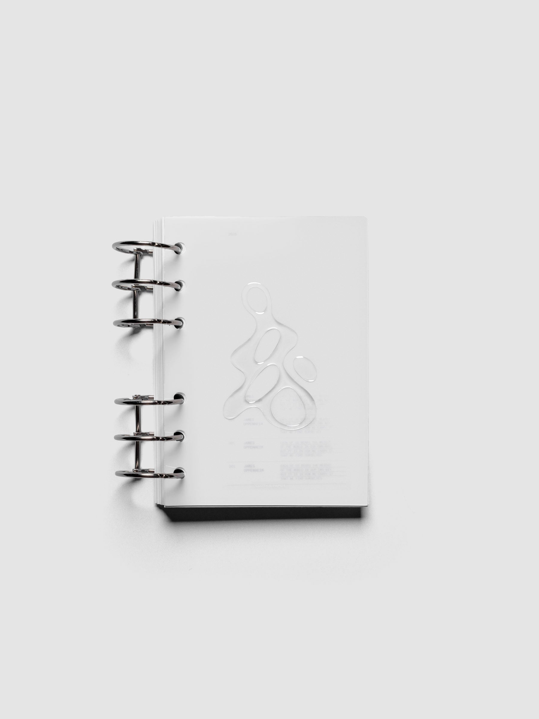 Light grey, semi-transparent, and glossy plastic planner dashboard with organic raised shape design in size A6 shown ringbound.