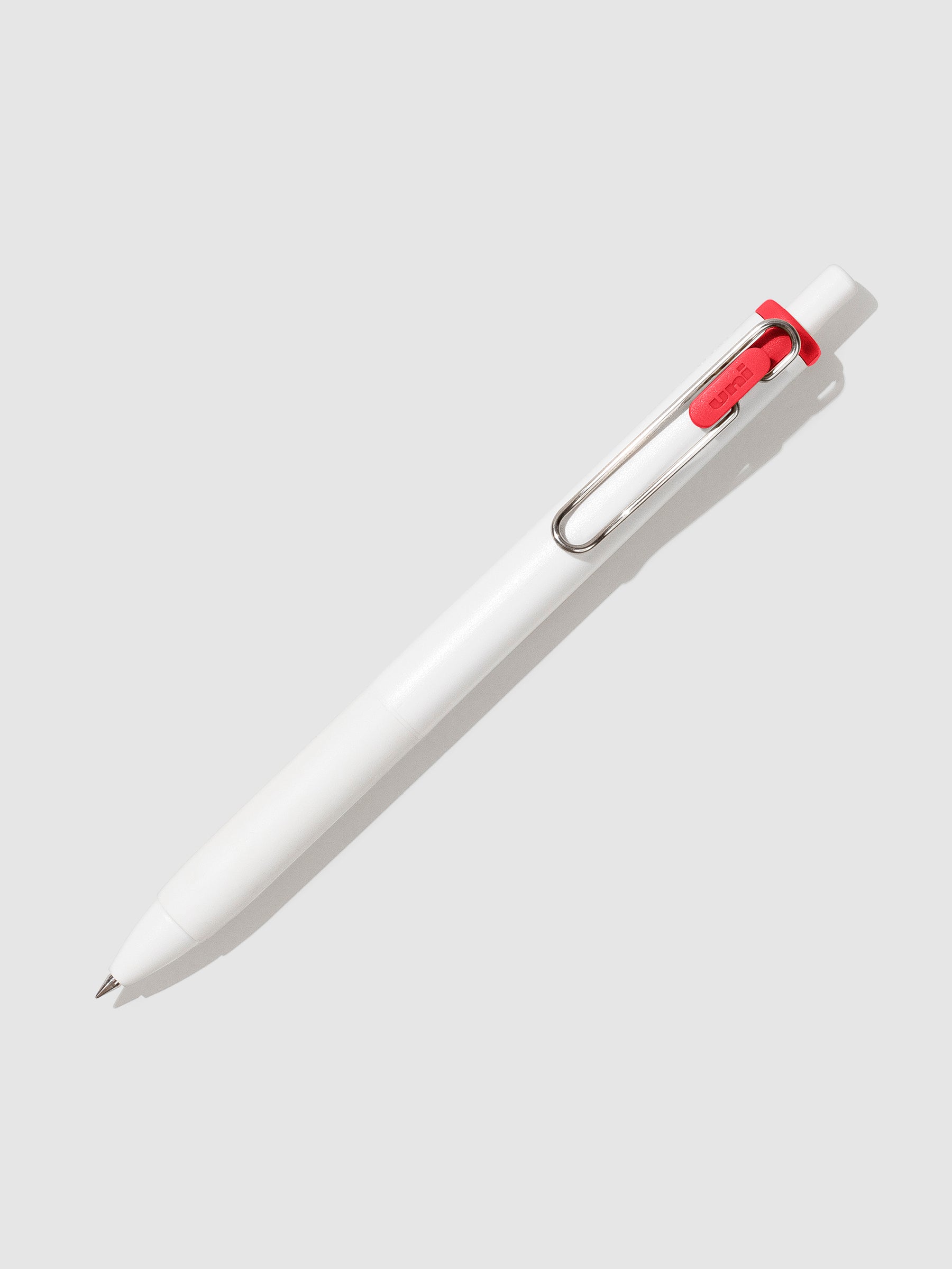 Uni-ball One Gel Pen, Red, Cloth and Paper. Pen tilted slightly to the right on a neutral background.