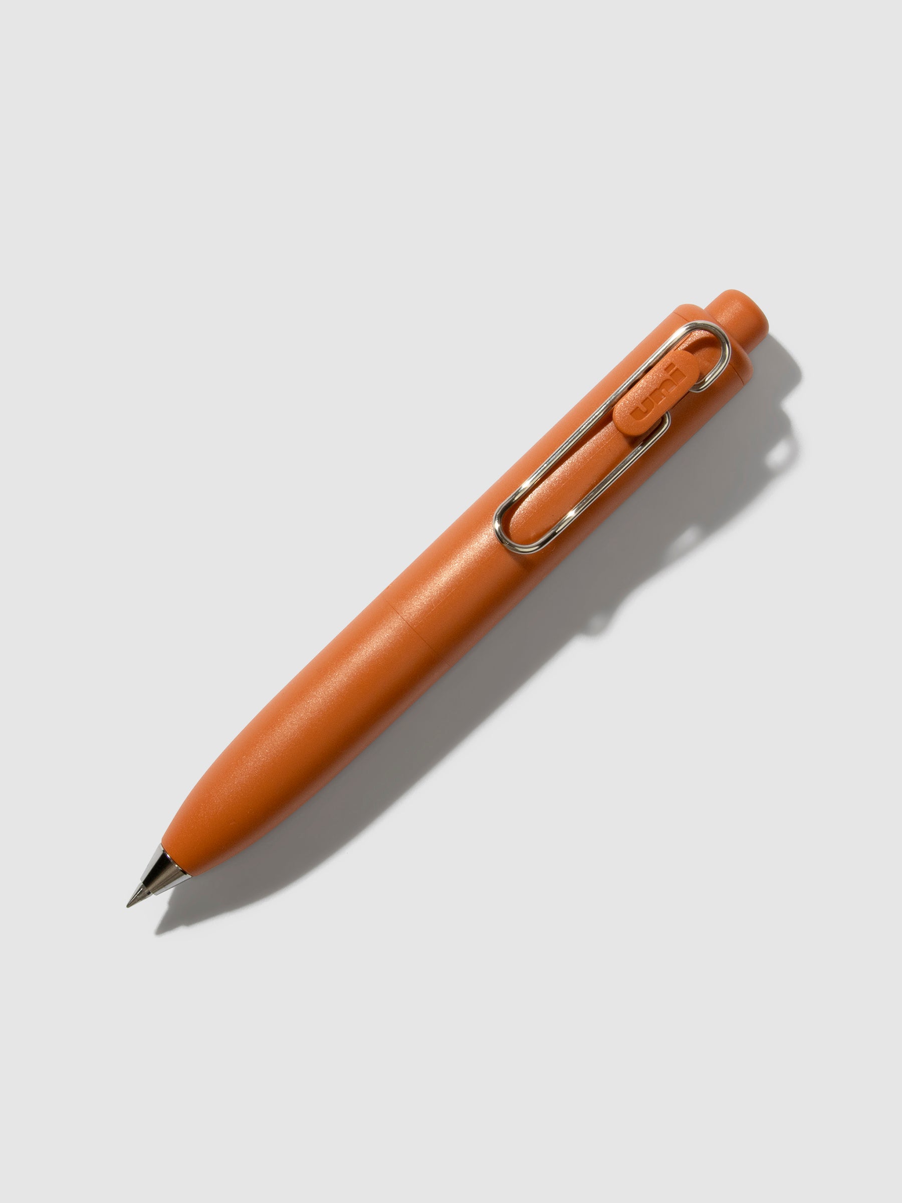 Uni-Ball One P Gel Pen, Cloth and Paper. Pen turned to the right on a neutral background. Color pictured is Mandarin Orange.