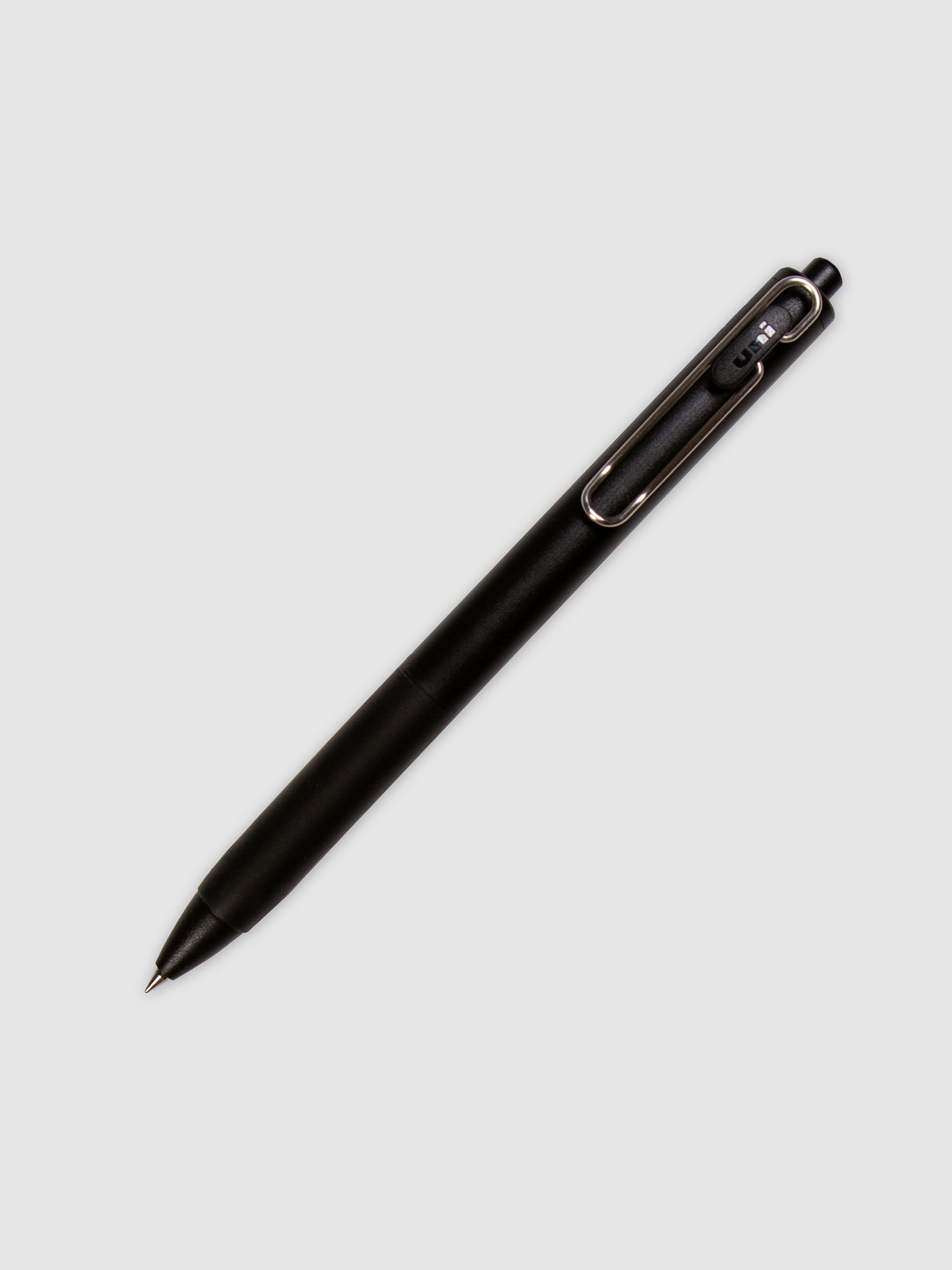 Uni One Gel Pen, 0.38 mm, Black Ink, Black Barrel, Cloth and Paper. Pen with nib exposed turned to the right against a neutral background.